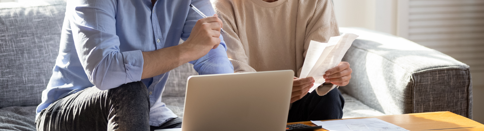 Couple paying bills sitting on a couch with a laptop